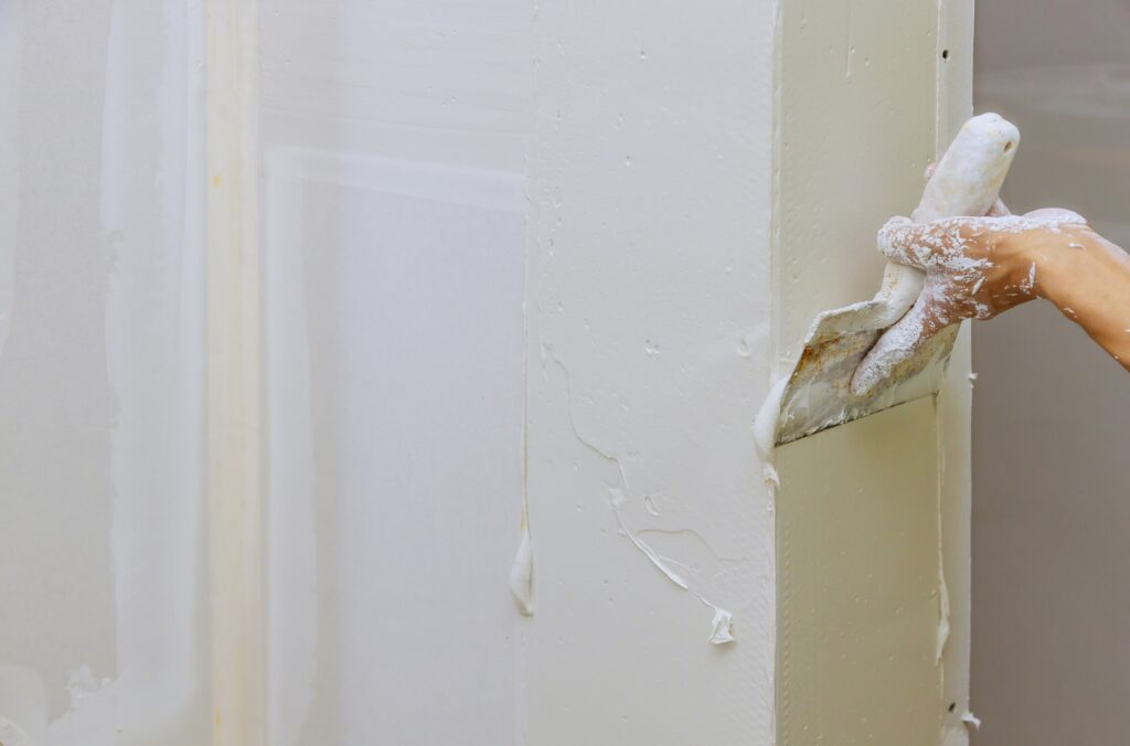 A Professional handyman is patching a drywall hole with joint compound.